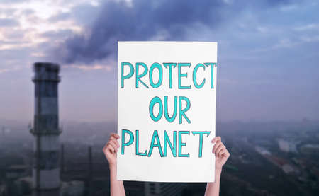 Protestor holding placard with text Protect Our Planet and blurred view of industrial factory on backgroundの写真素材