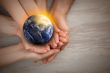 World in our hands. Top view of parents and kid holding digital model of Earth on wooden background, space for textの写真素材