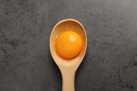 Wooden spoon with raw egg yolk on gray table, top viewの写真素材