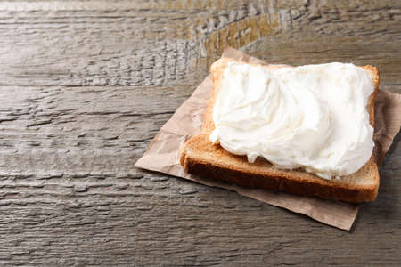 Slice of bread with tasty cream cheese on wooden table, space for textの写真素材