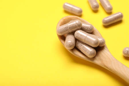 Gelatin capsules in spoon on yellow background, closeup. Space for textの写真素材