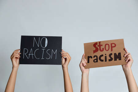 Women holding signs on gray background, closeup. Racism concept