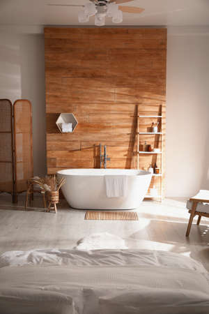 Stylish apartment interior with white bathtub and bedの写真素材