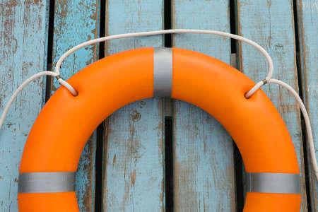 Orange life buoy on light blue wooden background, top view