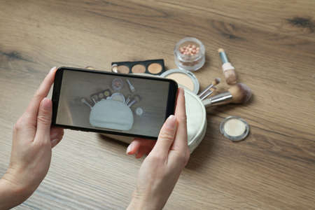 Woman taking photo of makeup products with smartphone at wooden table, closeupの写真素材