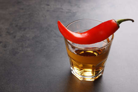 Red hot chili pepper and vodka in glass on gray table, space for textの写真素材