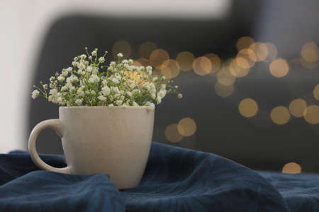 Cup with tiny flowers on soft knitted blanket against blurred lights. Space for textの写真素材
