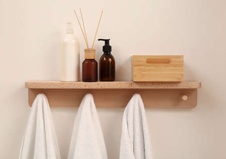 Wooden shelf with towels, soap dispensers and aromatic reed freshener on beige wall. Interior elementの写真素材
