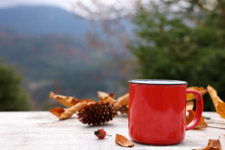 Mug of hot drink and autumn leaves on wooden table outdoors. Space for textの写真素材