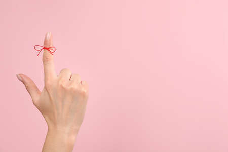 Woman showing index finger with tied red bow as reminder on pink background, closeup, Space for textの写真素材
