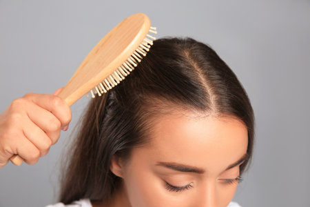 Woman with hair loss problem on gray background, closeup. Trichology treatment