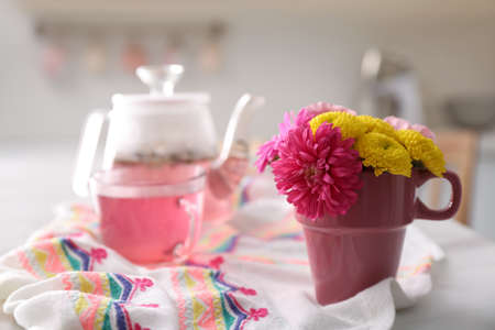 Beautiful bright flowers in pink cup, fabric and aromatic tea on table indoors, space for textの写真素材