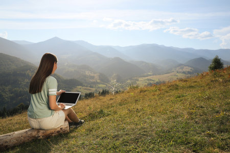 Young woman working with laptop in mountains on sunny dayの写真素材