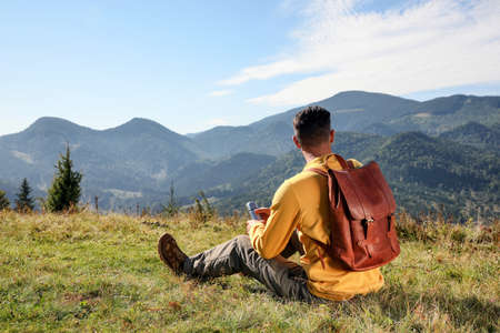 Tourist with flask and backpack enjoying beautiful mountain landscape, back view.