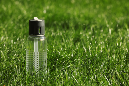 Sport bottle of water on green grass, space for textの写真素材