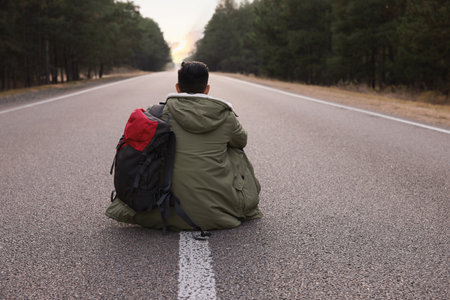 Man with backpack sitting on road near forest, back viewの写真素材