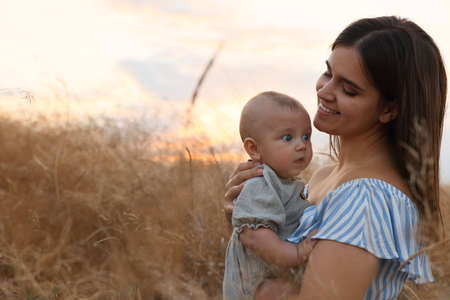Happy mother with adorable baby in field at sunset, space for textの写真素材