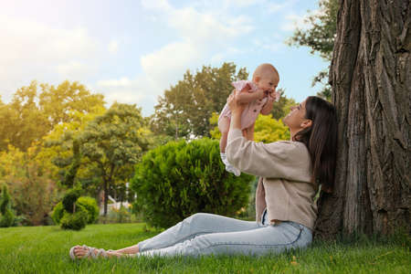 Happy mother with adorable baby sitting on green grass in parkの写真素材