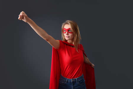 Confident woman wearing superhero cape and mask on gray backgroundの写真素材