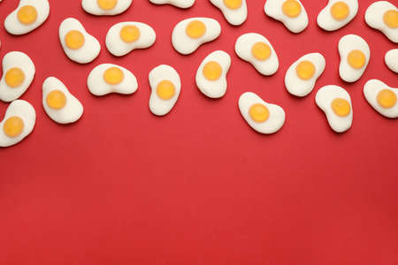 Tasty jelly candies in shape of egg on red background, flat lay. Space for text