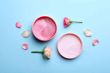 Under eye patches in jar and rose flowers on light blue background, flat lay. Cosmetic productの写真素材