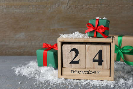 December 24 - Christmas Eve. Wooden block calendar and gift boxes on gray table, space for textの写真素材