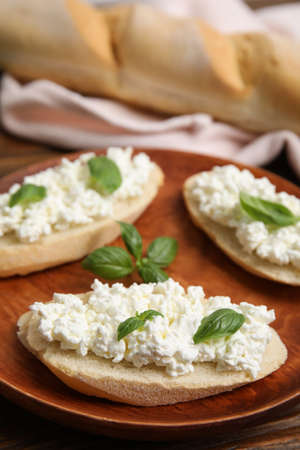 Bread with cottage cheese and basil on wooden plate, closeupの写真素材
