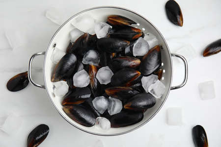 Colander with raw mussels and ice on white marble table, flat layの写真素材