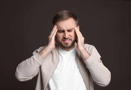 Young man suffering from headache on dark background