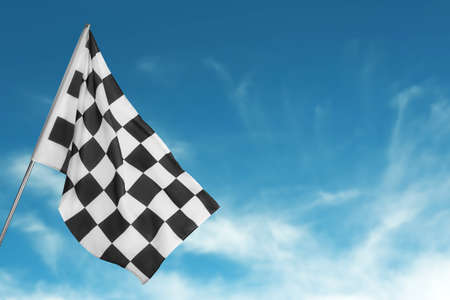 Checkered racing finish flag against blue sky. Space for text