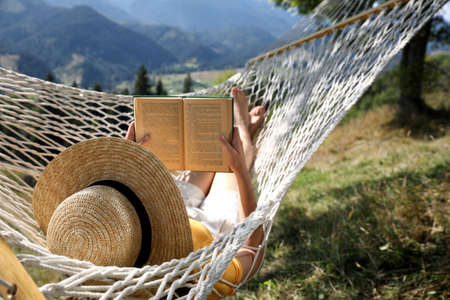 Young woman reading book in hammock outdoors on sunny dayの写真素材