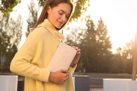 Fashionable young woman with stylish bag on city street. Space for text