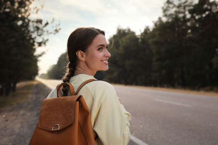 Young woman with backpack on road near forestの写真素材