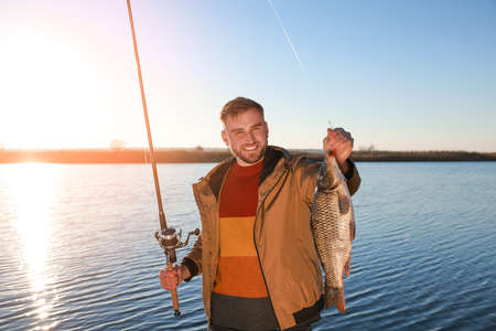 Fisherman holding fishing rod and catch at riverside