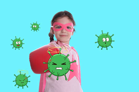 Cute little girl wearing superhero costume and boxing gloves fighting against viruses on turquoise backgroundの写真素材