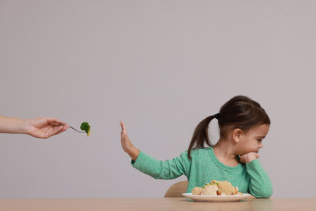 Cute little girl refusing to eat vegetables at table on gray backgroundの写真素材
