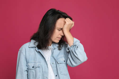 Mature woman suffering from headache on pink backgroundの写真素材