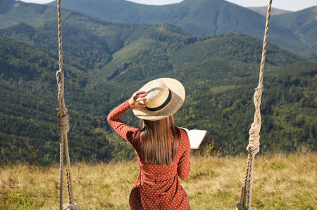 Young woman reading book in mountains, back viewの写真素材