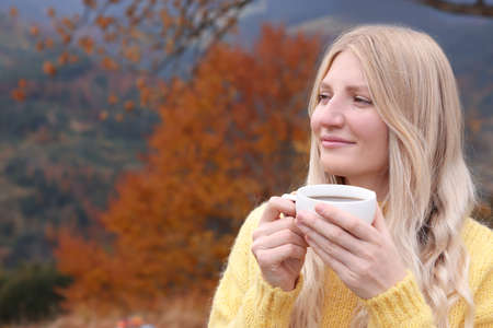 Young woman with cup of hot drink outdoors in autumn. Space for textの写真素材