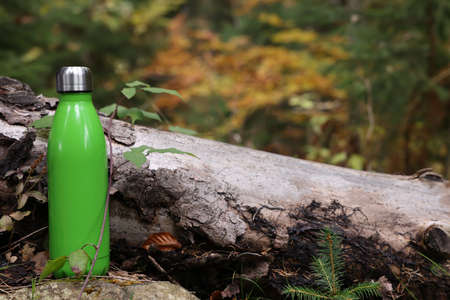 Green thermo bottle near log in forestの写真素材