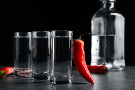 Red hot chili peppers and vodka on gray table against black backgroundの写真素材