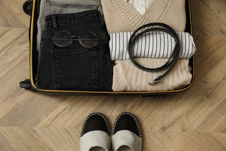 Open suitcase with folded clothes, accessories and shoes on floor, flat lay