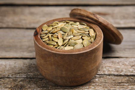 Dish with pumpkin seeds and lid on wooden table, closeupの写真素材