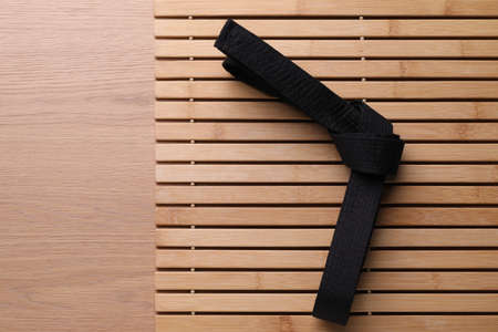 Tied black belt on wooden background, top view with space for text. Oriental martial artsの写真素材