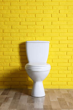 New clean toilet bowl near yellow brick wall indoors. Interior designの写真素材