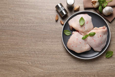 Raw chicken thighs with basil on wooden table, flat lay. Space for textの写真素材