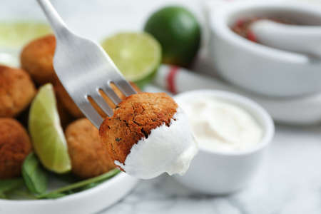 Fork with delicious falafel ball and sauce over table, closeupの写真素材