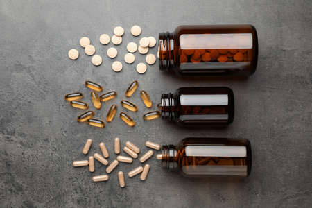Overturned bottles with different dietary supplements on gray table, flat layの写真素材