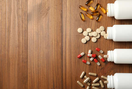Overturned bottles with different dietary supplements on wooden table, flat lay. Space for textの写真素材