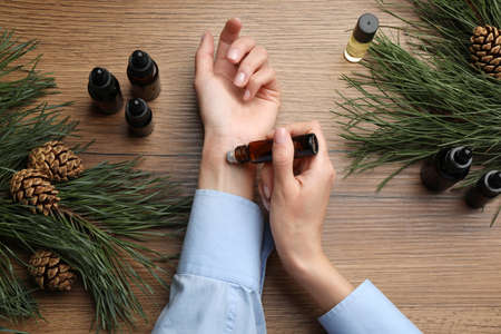 Woman applying pine essential oil on wrist at wooden table, top viewの写真素材